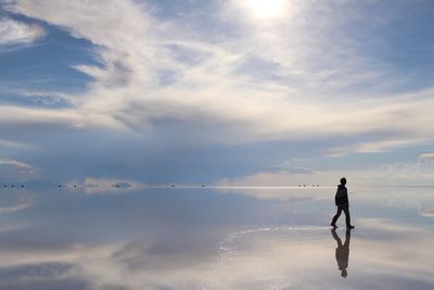 Man walking on salt flat against sky at salar de uyuni