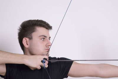 Close-up of young man holding camera against white wall