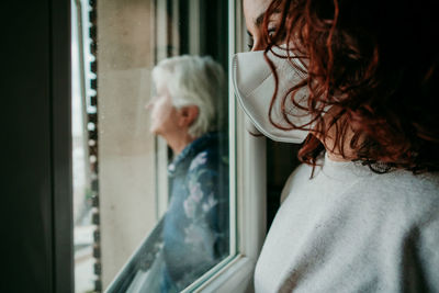 Rear view of woman looking through window at home