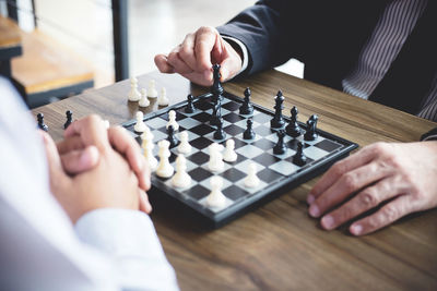 Midsection of business people playing chess on wooden table in office