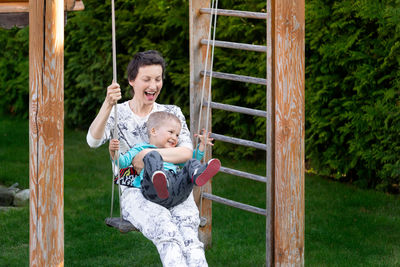 Cheerful woman with son swinging at park