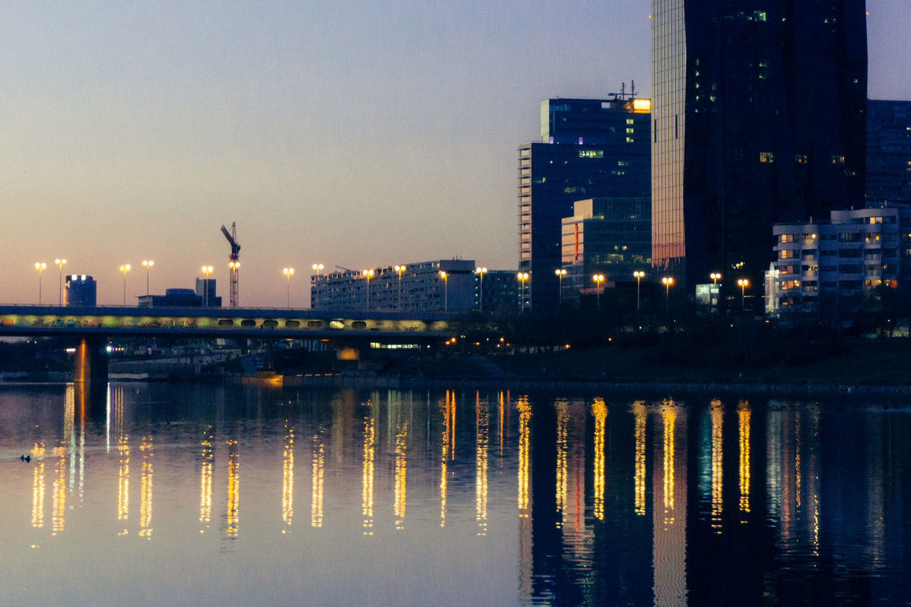 ILLUMINATED BUILDINGS BY RIVER AGAINST SKY