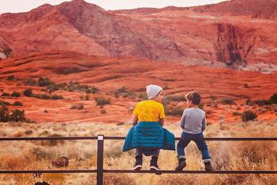 Boys sitting on fence, talking to each other by the sandstone cliffs