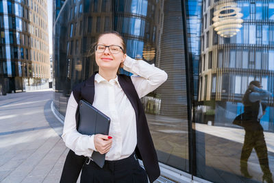 Business caucasian woman holding a laptop and outdoors surrounded by buildings.