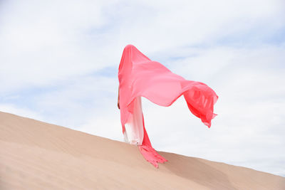 Caucasian woman standing in desert against blue sky, covered with pink fabric. face not visible. 