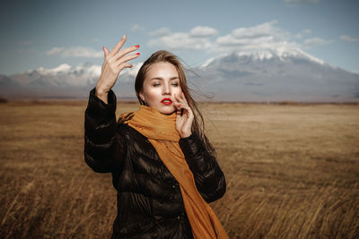 Portrait of young woman standing on field against sky