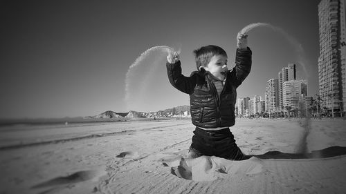 Boy playing with sand on beach against clear sky