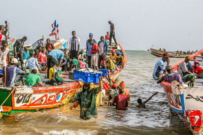 People by boats in sea against sky