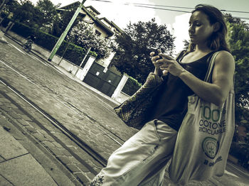 Young woman using phone while standing on tree