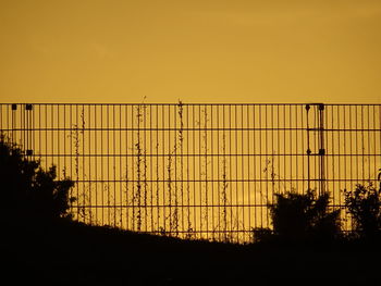 Silhouette fence against orange sky