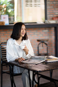 Young woman using mobile phone while sitting at cafe