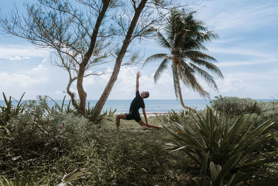 Full length of a yoga pose by tree against sky