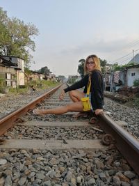 Portrait of smiling young woman on railroad track against sky