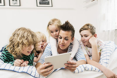 Mother and children using digital tablet lying in bed at home