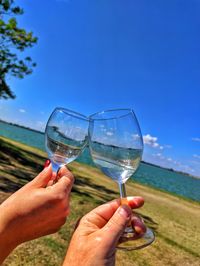 Cropped image of hand holding drink against blue sky