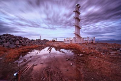 Lighthouse on beach against cloudy sky