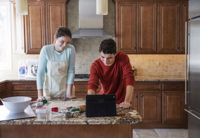 Happy siblings using laptop computer in kitchen at home