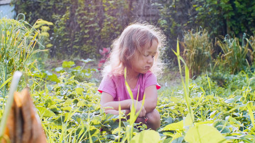 Girl looking away while crouching amidst plants