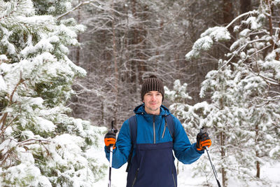 Skier with a backpack and hat with pompom with ski poles in his hands on background of a snowy 