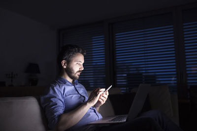Man working at night using smart phone and laptop