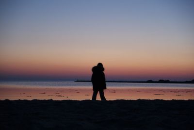 Silhouette woman standing on beach against clear sky during sunset