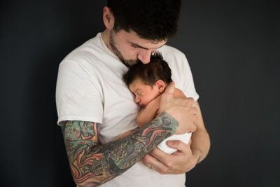 Tattooed millennial dad kisses newborn son wearing diaper