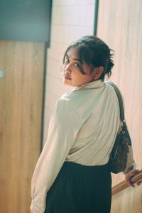 Side view of young woman standing against wall