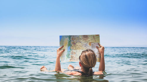 Full length of woman holding map while swimming in dead sea