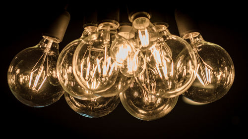 Close-up of illuminated light bulb hanging against black background