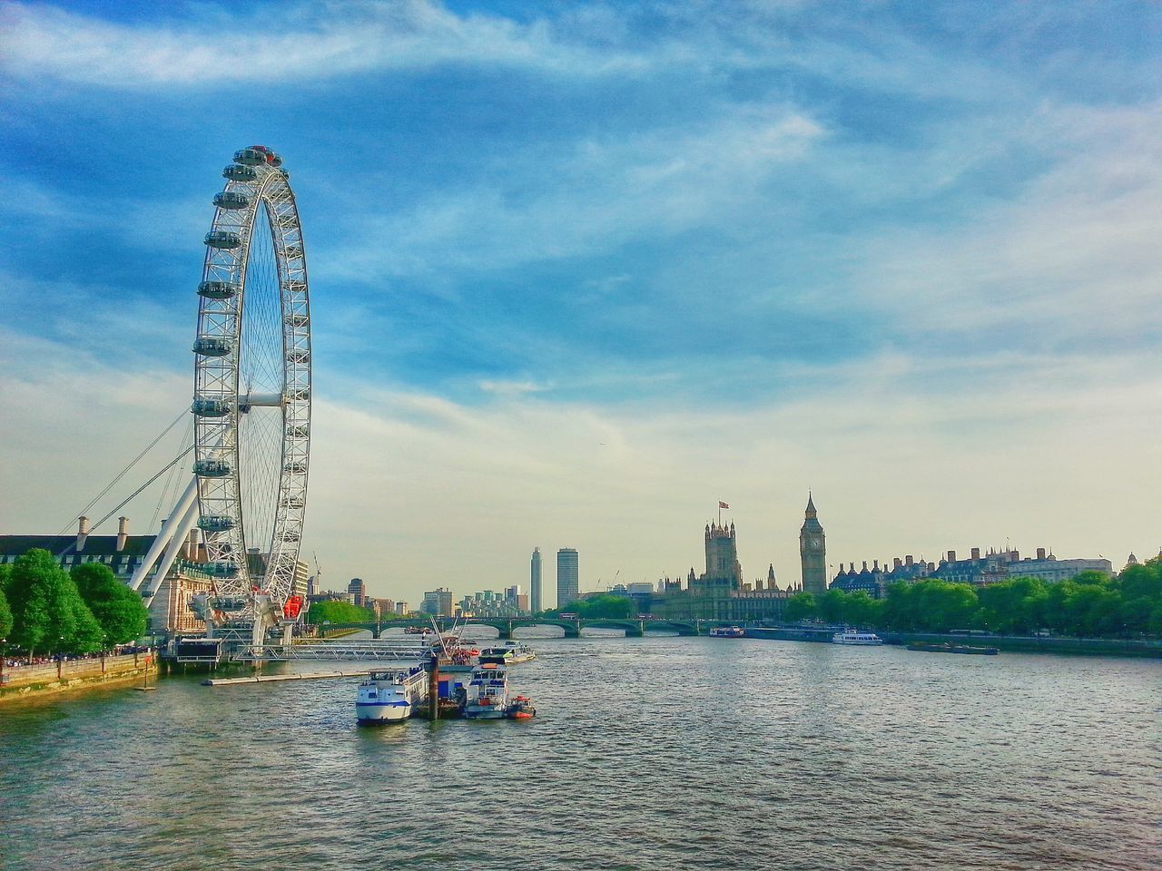 sky, waterfront, water, ferris wheel, built structure, architecture, river, cloud - sky, amusement park ride, travel destinations, tourism, amusement park, famous place, travel, tall - high, international landmark, arts culture and entertainment, nautical vessel, building exterior, cloud