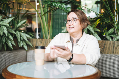 Adult middle aged woman plus size in casual clothes with coffee using mobile phone in cafe