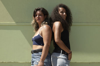 Portrait of two young women standing against green wall