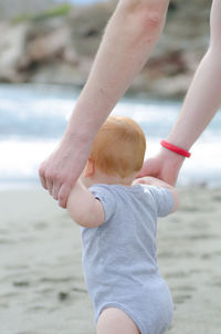 Cropped hands of parent holding son at beach