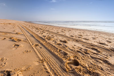 Footprints on sand at beach against sky