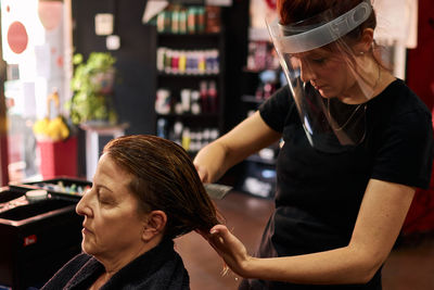 Hairdresser combs a client with a face shield