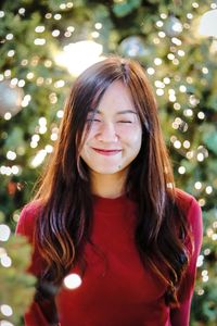 Smiling young woman standing against christmas tree