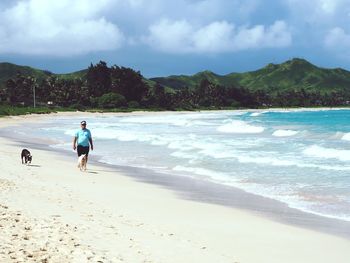 Rear view of man walking on beach against sky