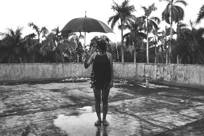 Full length of woman holding umbrella during rainy season at building terrace