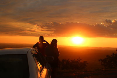 Rear view of friends with car looking at view during sunset
