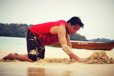 Side view of man playing on sand at beach against sky