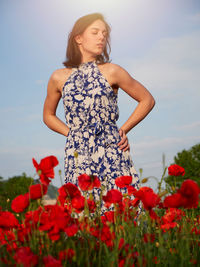 Portrait of young woman standing amidst flowering plants against sky