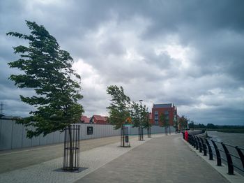 Empty footpath amidst buildings in city against sky