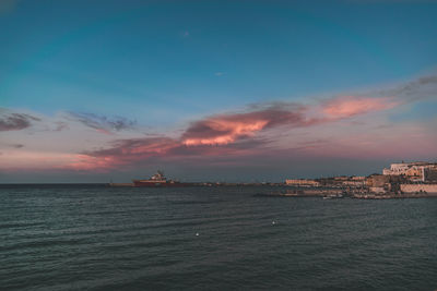 Scenic view of sea by buildings against sky during sunset