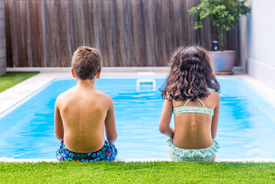 Two little kids on the edge of the swimming pool. rear view