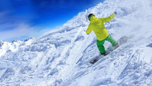 Rear view of young man skiing on snowcapped mountain against sky