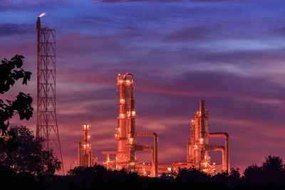 Low angle view of illuminated factory against sky during sunset