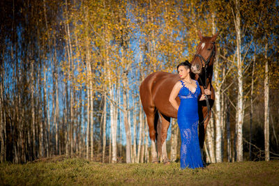 Woman standing by horse at forest during autumn