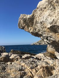 Rock formations on shore against clear blue sky