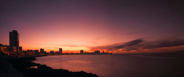 Silhouette buildings by sea against romantic sky at sunset