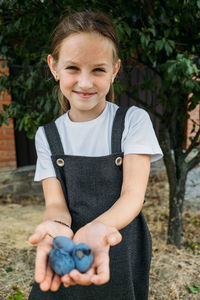 Candid portrait of preschooler girl in plum tree orchard. girl holding fresh plums. kids picking 